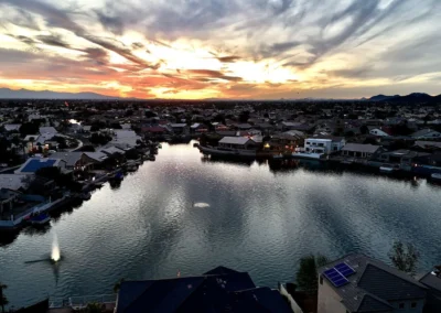 A suburban neighborhood with houses surrounding a reflective lake at sunset, under a sky with dramatic clouds.